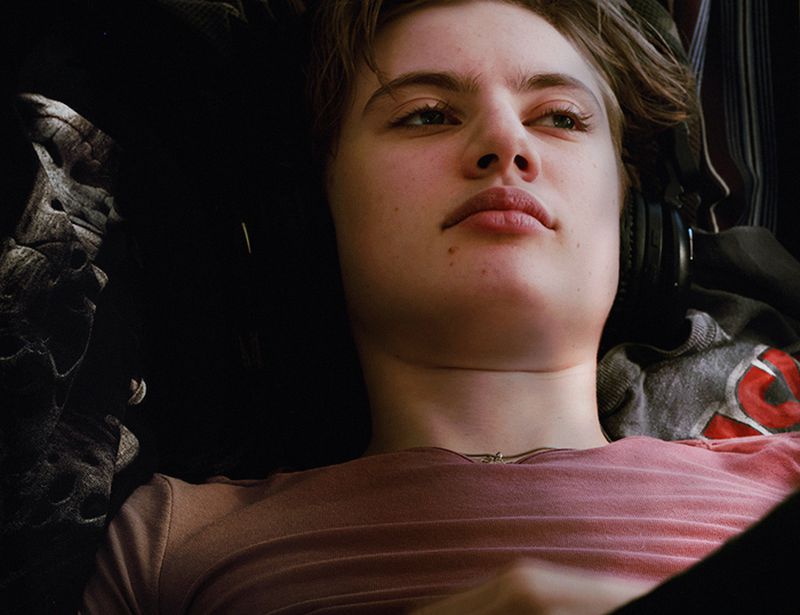 Portrait of a young adult woman with short hair, wearing a pink shirt and silver necklace while lying down, looking up and to the right.