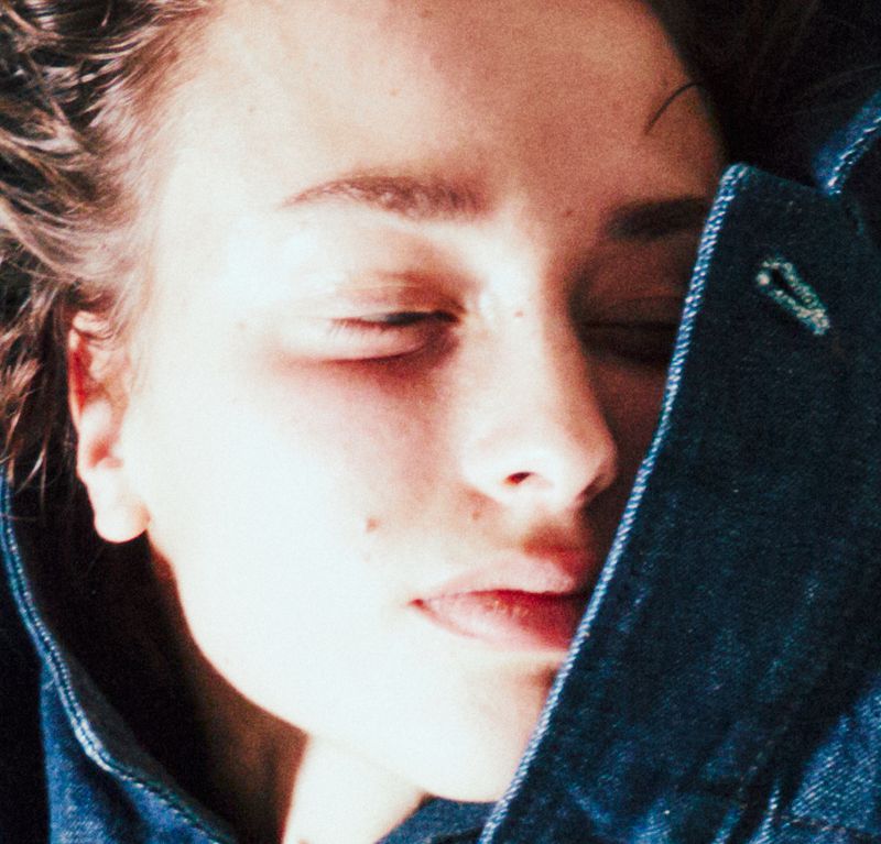 Close-up portrait of a young adult female with closed eyes wearing a denim jacket, capturing a serene and peaceful expression.