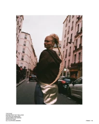 Model in a brown hoodie walking down a narrow urban street lined with traditional apartment buildings.
