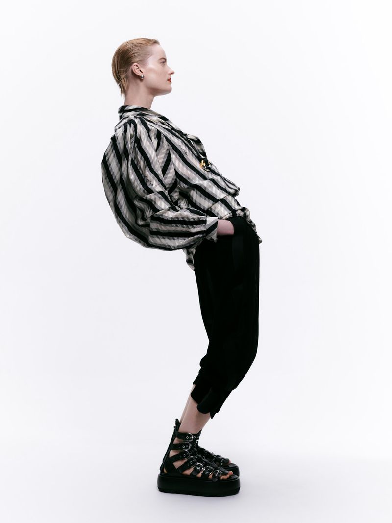 Model in a black and white striped blouse and black trousers posing against a clean white backdrop