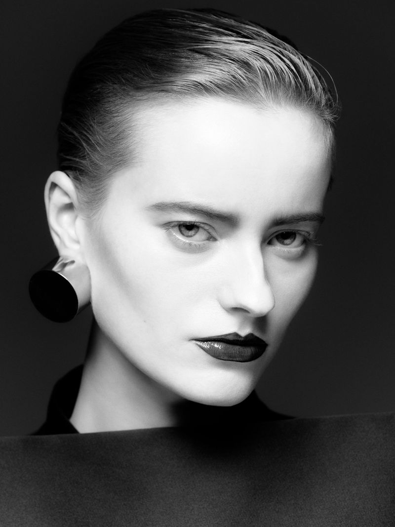 Striking black and white portrait of an adult woman with slicked-back hair, dark lipstick, and modern disc earring against a dark backdrop.