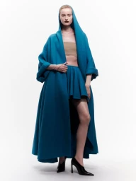 Model wearing a long blue hooded coat and skirt set against a white seamless background for Puss Puss Magazine