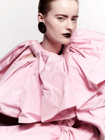 Model wearing a voluminous pink ruffled top and dark earrings against a white background for Puss Puss Magazine