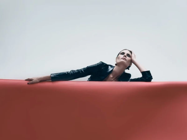 Model Adina Fohlin posing in a dark leather jacket behind a curved red roll against a plain white background