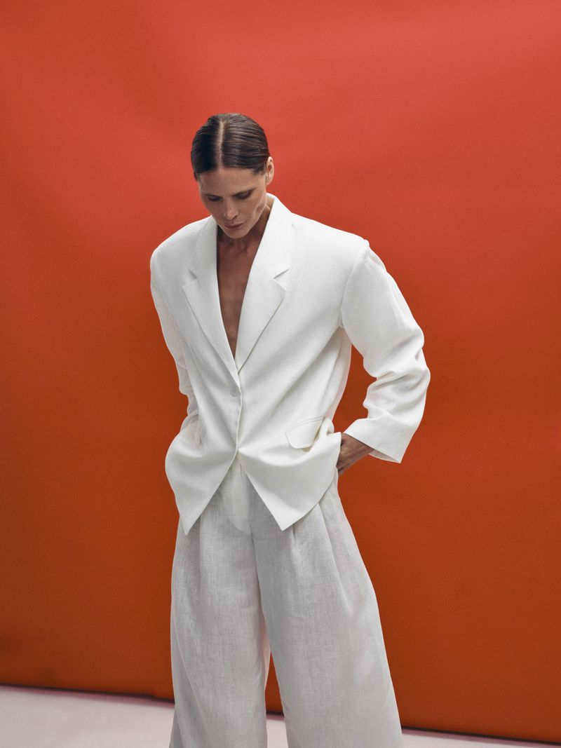 Model Adina Fohlin in a white blazer and trousers standing against a vibrant red backdrop for Faith Love Hope Magazine.