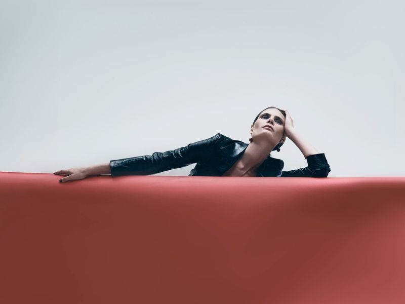 Model Adina Fohlin posing in a dark leather jacket behind a curved red roll against a plain white background