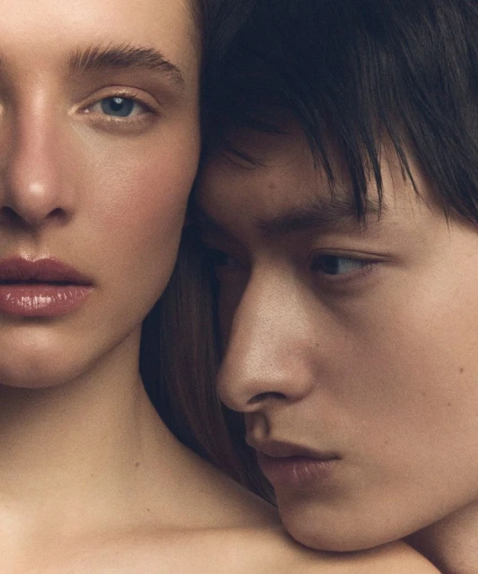 Close-up portrait of an adult Caucasian female and an Asian male with short dark hair, facing the camera indoors in neutral lighting.