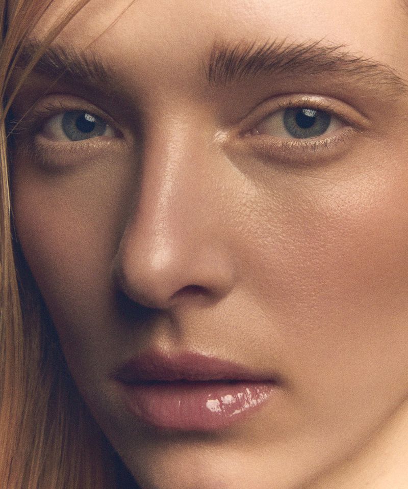 Close-up portrait of a young adult woman with light skin and blue eyes, soft pink lips, and blonde hair, evenly lit in a studio setting.