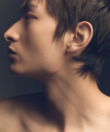 Close-up profile portrait of a model with short dark hair against a dark studio background
