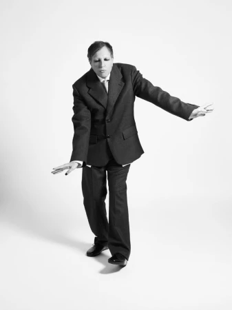 Man wearing a dark suit with arms outstretched posing against a plain white background