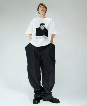 Model wearing a white graphic t-shirt and black trousers against a plain white studio background