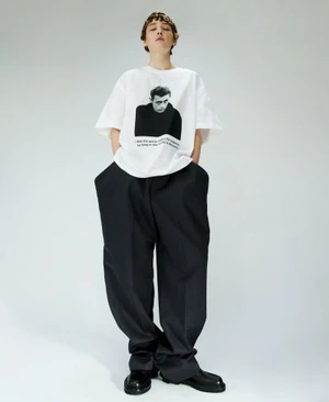 Model wearing a white graphic t-shirt and black trousers against a plain white studio background