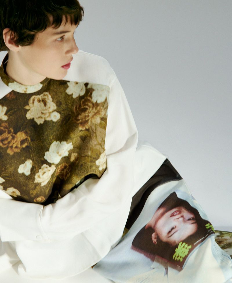 Model with short dark hair wearing a white top with a floral panel against a light grey background