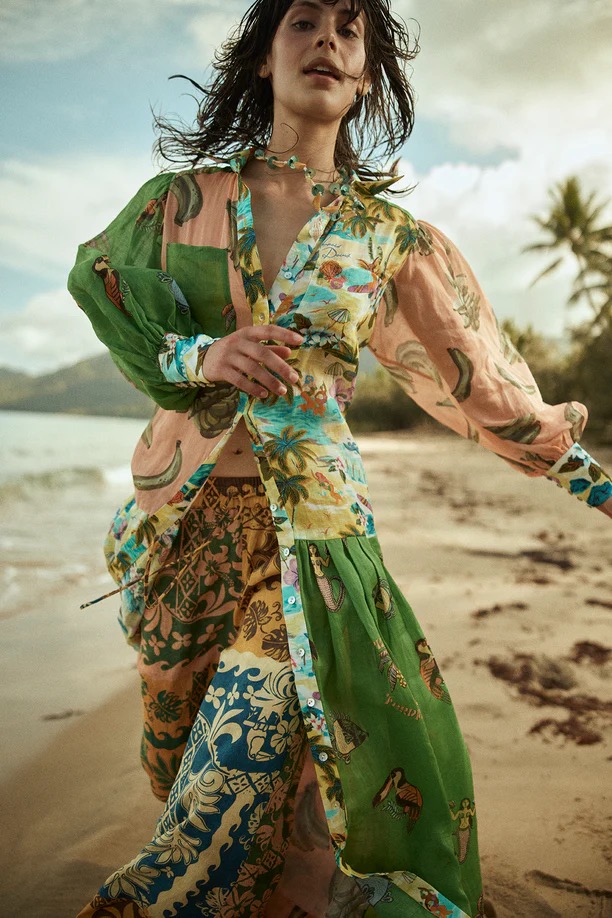 Woman in colorful, patterned maxi dress on a tropical beach. She is walking towards the camera with palm trees and water behind her.