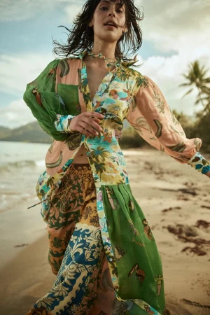 Woman in colorful, patterned maxi dress on a tropical beach. She is walking towards the camera with palm trees and water behind her.