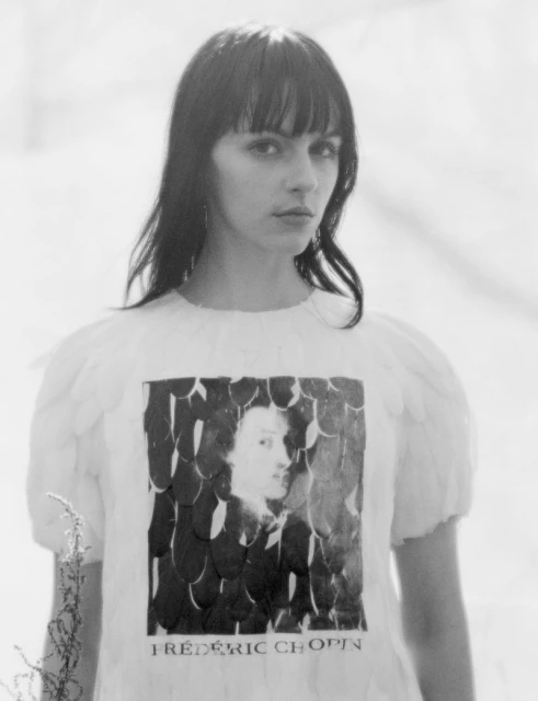 Monochromatic portrait of a woman wearing a feathered dress with a Chopin graphic, set against a soft, blurred, light-toned background.