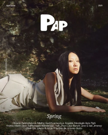 Model with long dark hair lying on mossy ground wearing a beige sleeveless top for PAP Magazine