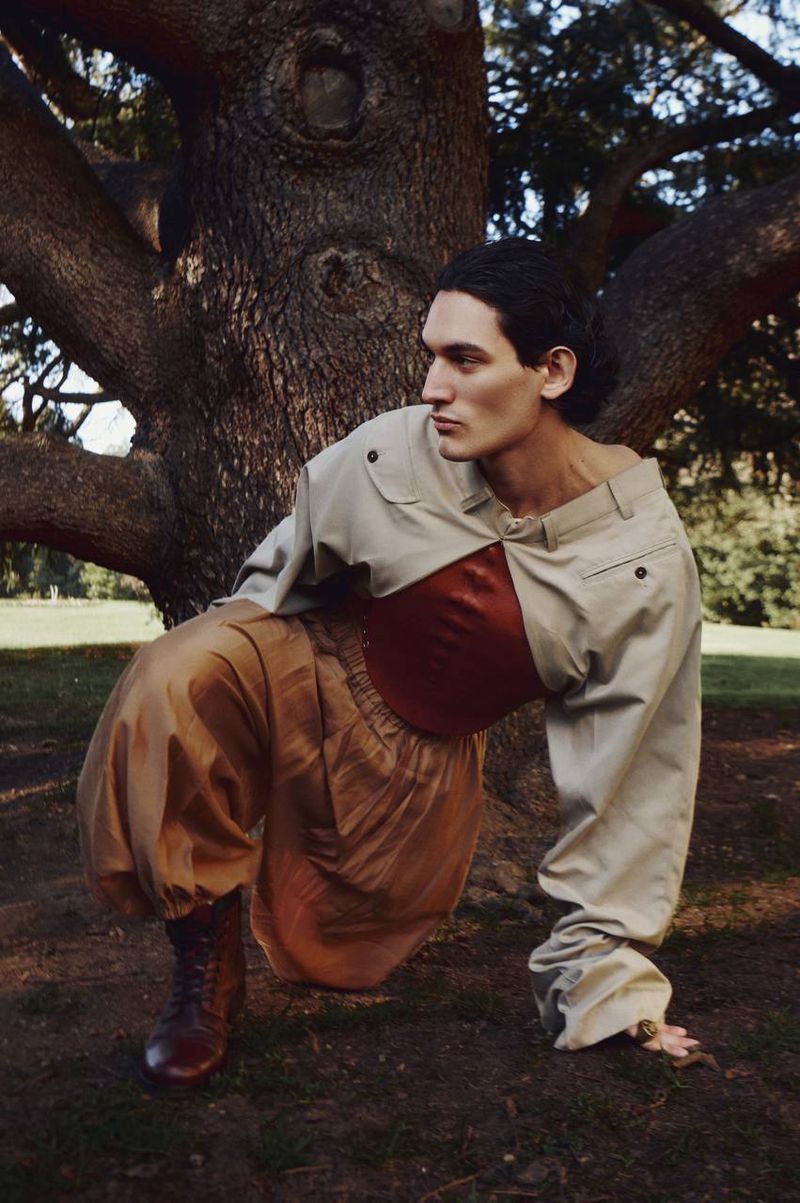 Model crouching by a tree trunk wearing a structured beige top and voluminous tan trousers for PAP Magazine