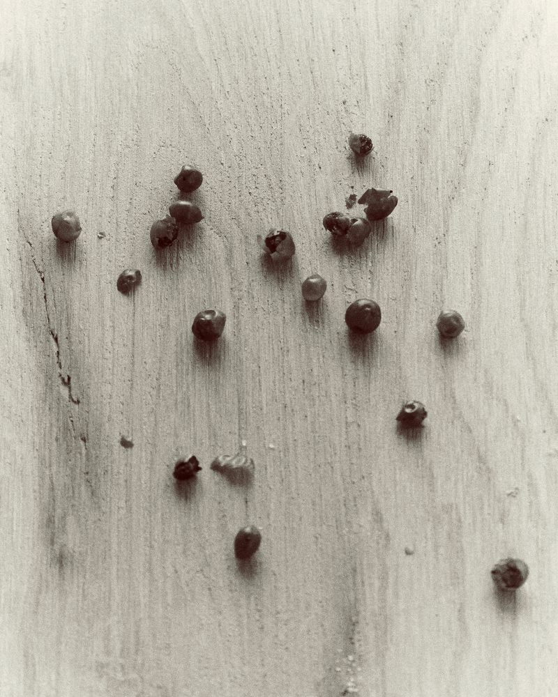 Scattered blueberries on a light brown wood surface, featuring varying sizes and conditions, with some berries intact and others crushed.