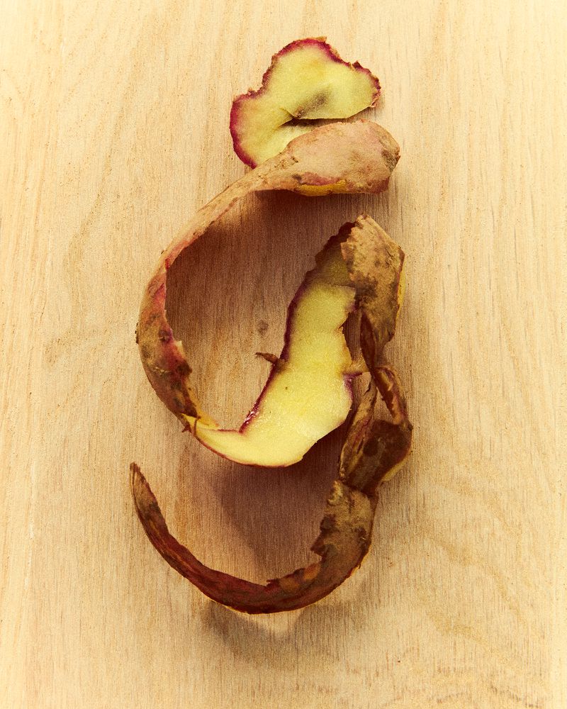 Close-up of sweet potato peel with curling texture on a light brown wood surface; studio lighting. Food photography.
