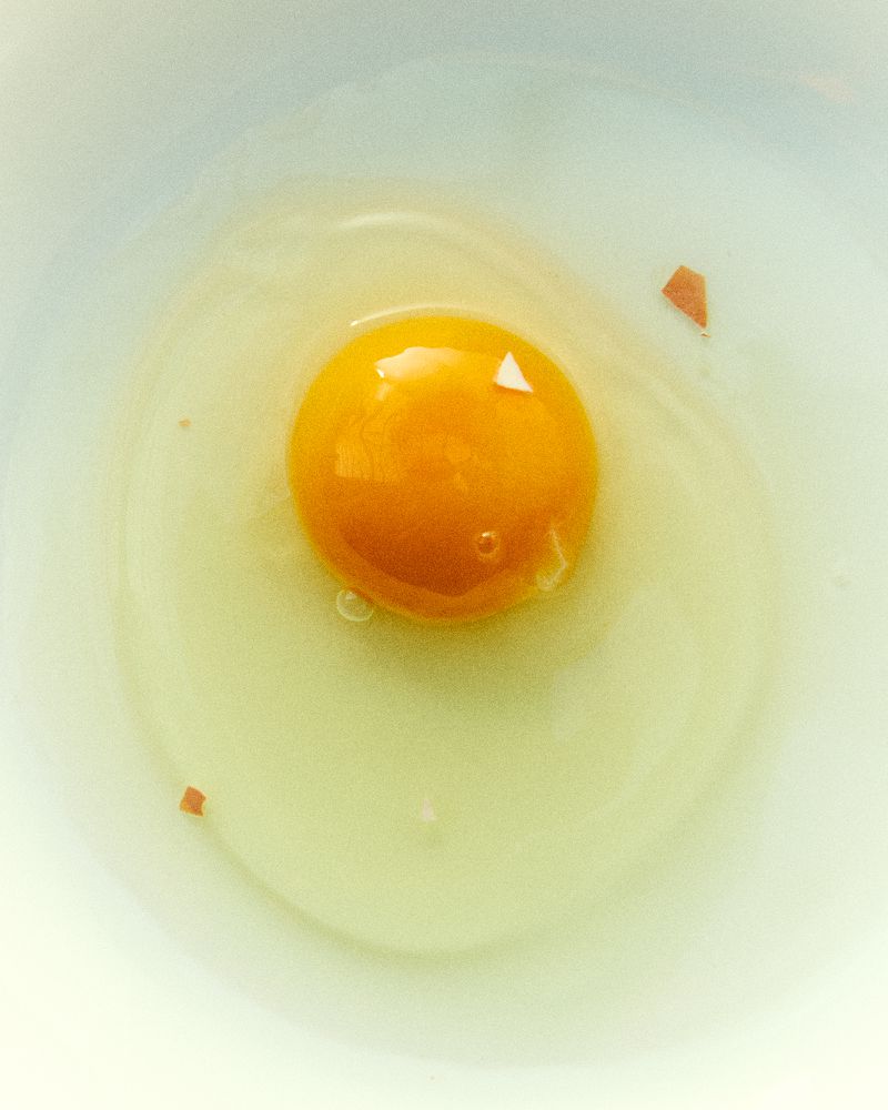 Overhead close-up shot of a raw egg with a bright yellow yolk sitting in the center of the egg white, inside a light blue bowl.