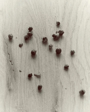 Scattered peppercorns on a light wood grain surface captured from above by Florent Tanet for A Magazine Curated By.