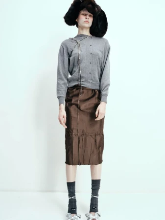 Model wearing a grey cardigan, brown satin skirt, furry black hat, and grey socks against a white backdrop.