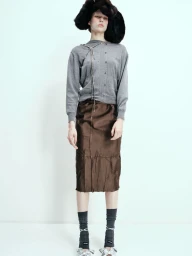 Model wearing a grey cardigan, brown satin skirt, furry black hat, and grey socks against a white backdrop.