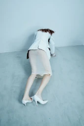 Model in a white blazer and sheer skirt crouched on a grey seamless floor for Self Service