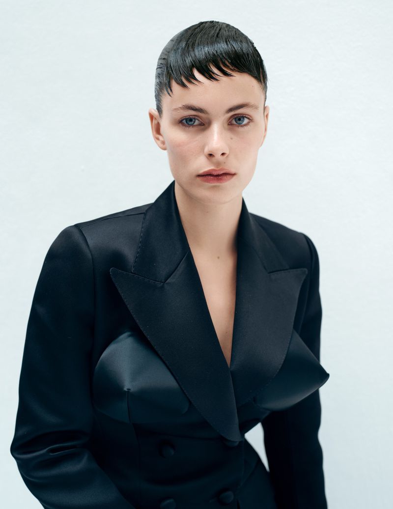 Close-up portrait of a woman in a black satin blazer against a white background in a fashion photography style, with minimal retouching.