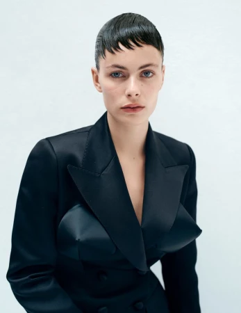 Model with short wet-look hair wearing a black sculpted blazer against a plain white background