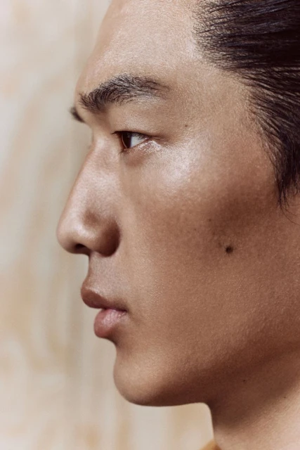 Close-up profile of an Asian adult male's face with smooth skin, neutral expression, and a tan complexion in a studio-style setting.