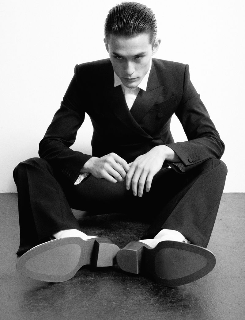 Model Alex Schlab seated in a dark suit with slicked hair for HERO Magazine, shot by Samuel Stephenson.