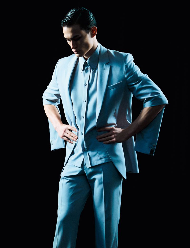 Model wearing a light blue suit and shirt standing against a dark background for HERO Magazine