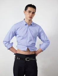Model wearing a light blue buttoned shirt and dark trousers against a white seamless background for HERO Magazine