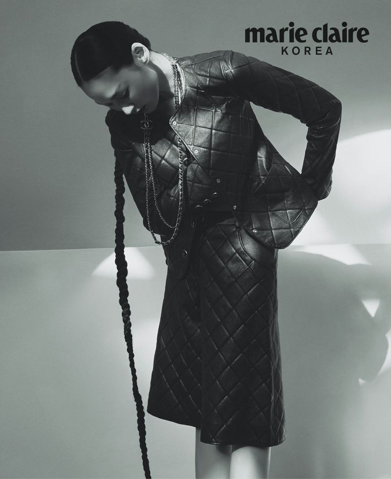 Marie Claire Korea cover featuring a woman in a black quilted jacket and skirt, looking down, with a long braid and a light gray background.