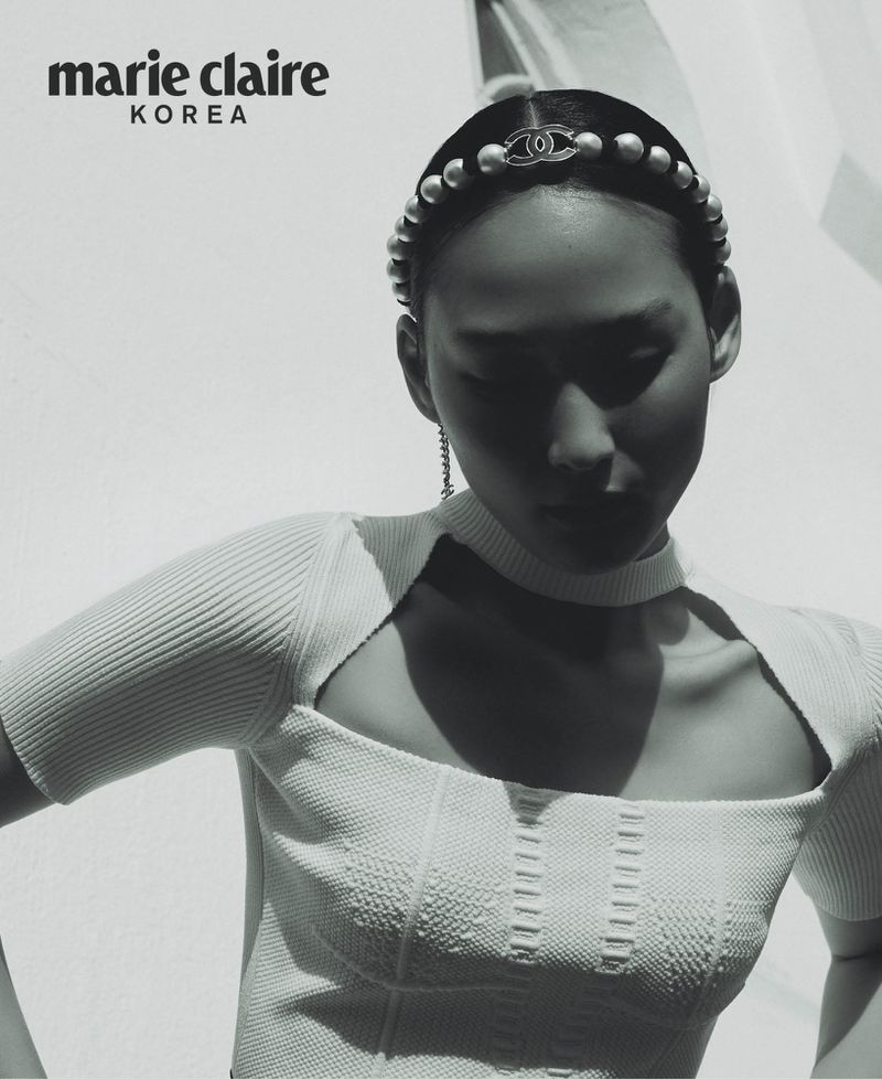 Black-and-white fashion editorial shot of an Asian woman wearing a pearl headband and white top, posing against a light background.