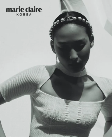 Black-and-white fashion editorial shot of an Asian woman wearing a pearl headband and white top, posing against a light background. 