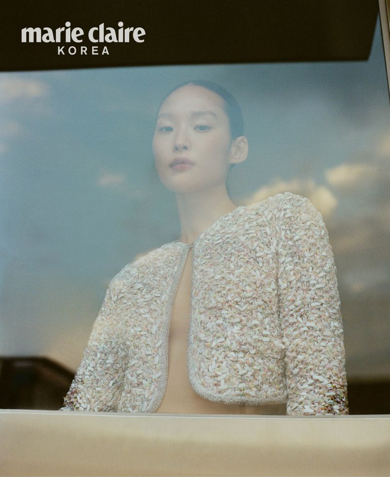Asian woman in a textured, cropped jacket poses in front of a window with a hazy sky; Marie Claire Korea logo is visible in the upper left.