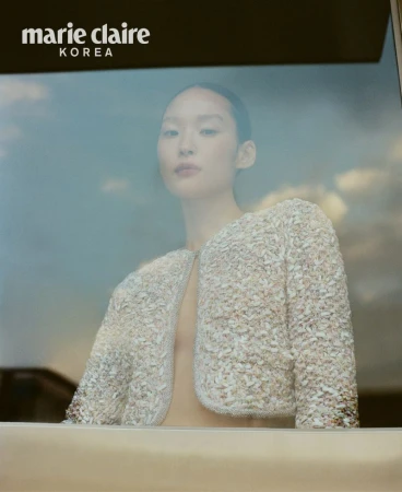 Asian woman in a textured, cropped jacket poses in front of a window with a hazy sky; Marie Claire Korea logo is visible in the upper left.