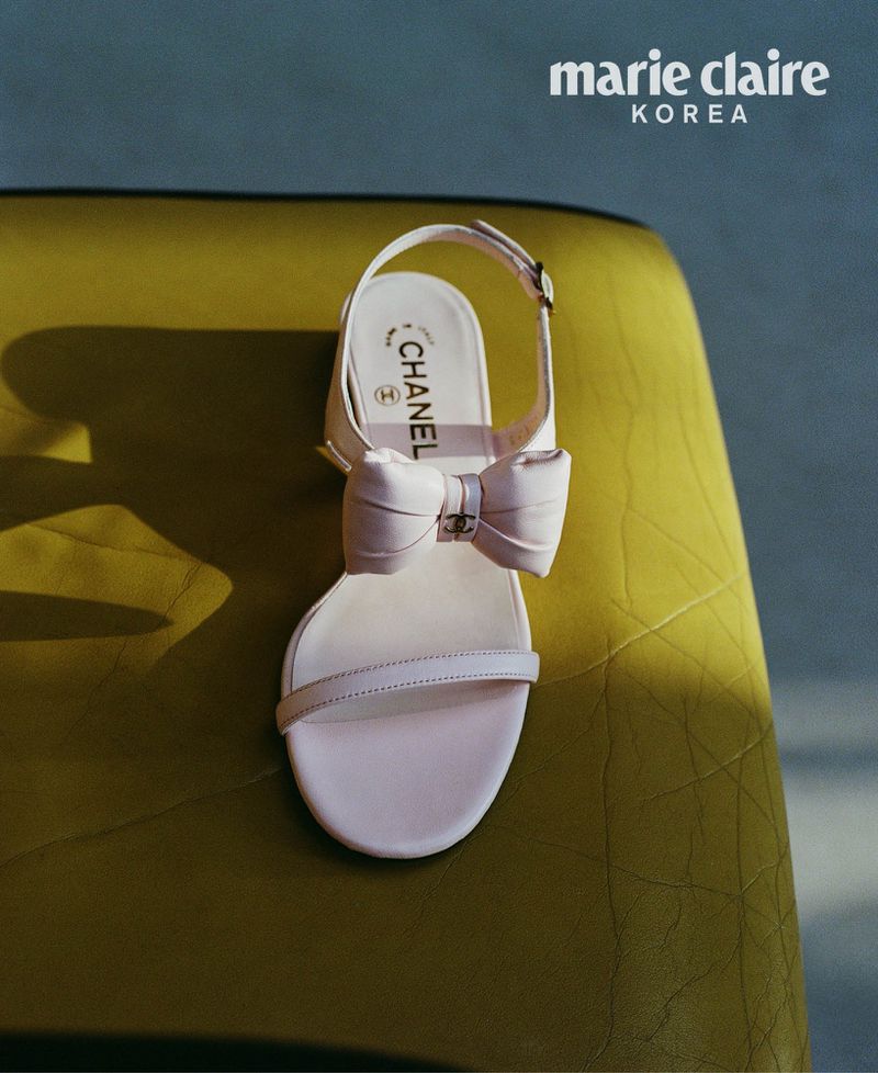 Elegant women's white leather heeled sandal with a bow by Chanel, resting on a textured chartreuse surface, fashion editorial.