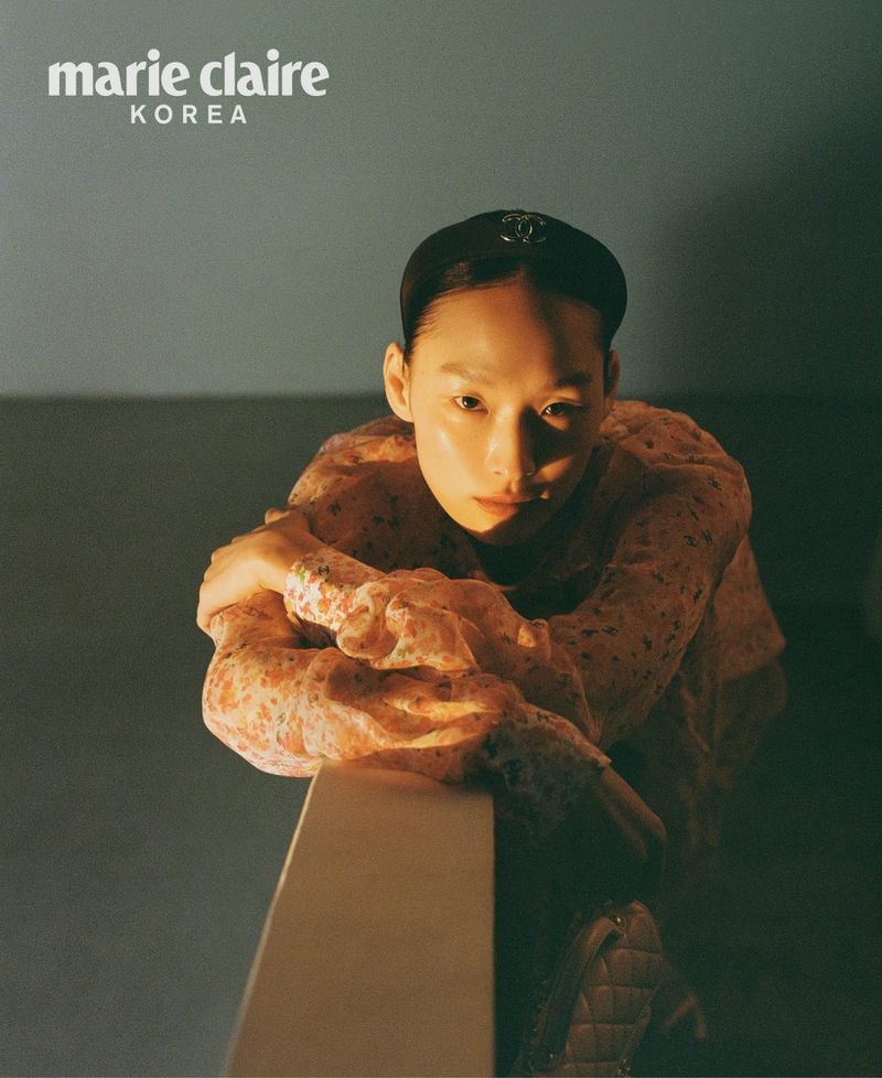 Elegant woman in floral dress and black headband poses indoors for Marie Claire Korea, captured with moody lighting.