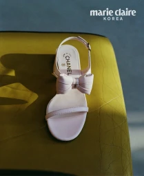 Close-up shot of a light pink Chanel slingback sandal with a prominent bow detail resting on a textured olive green surface.