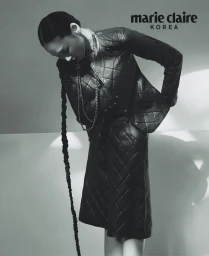 Model wearing a black quilted leather jacket and skirt with a long braided hair extension against a bright background.