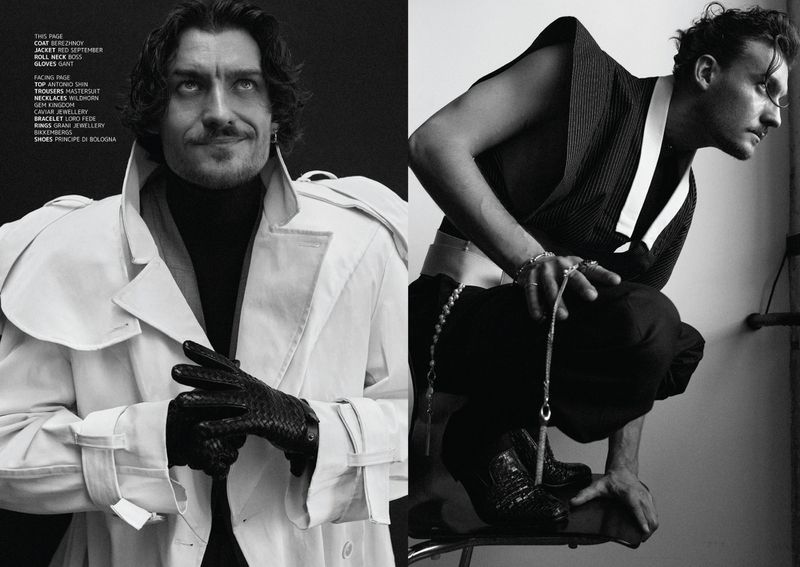 Two fashionable adult men in a monochrome fashion editorial. One poses in a white coat and gloves, the other in a sleeveless top.