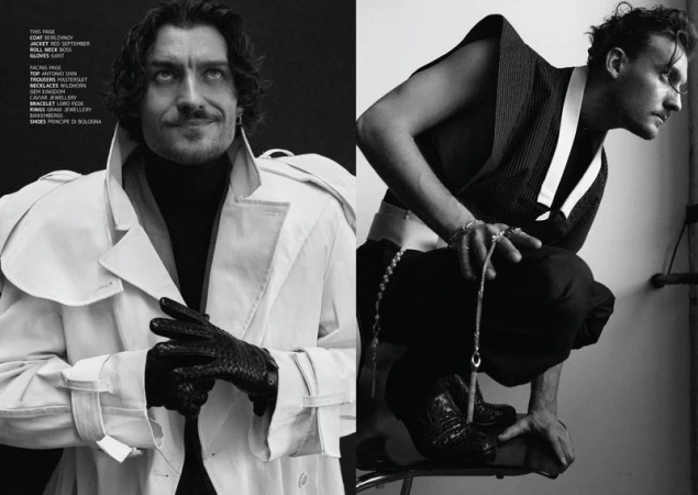 Two fashionable adult men in a monochrome fashion editorial. One poses in a white coat and gloves, the other in a sleeveless top.