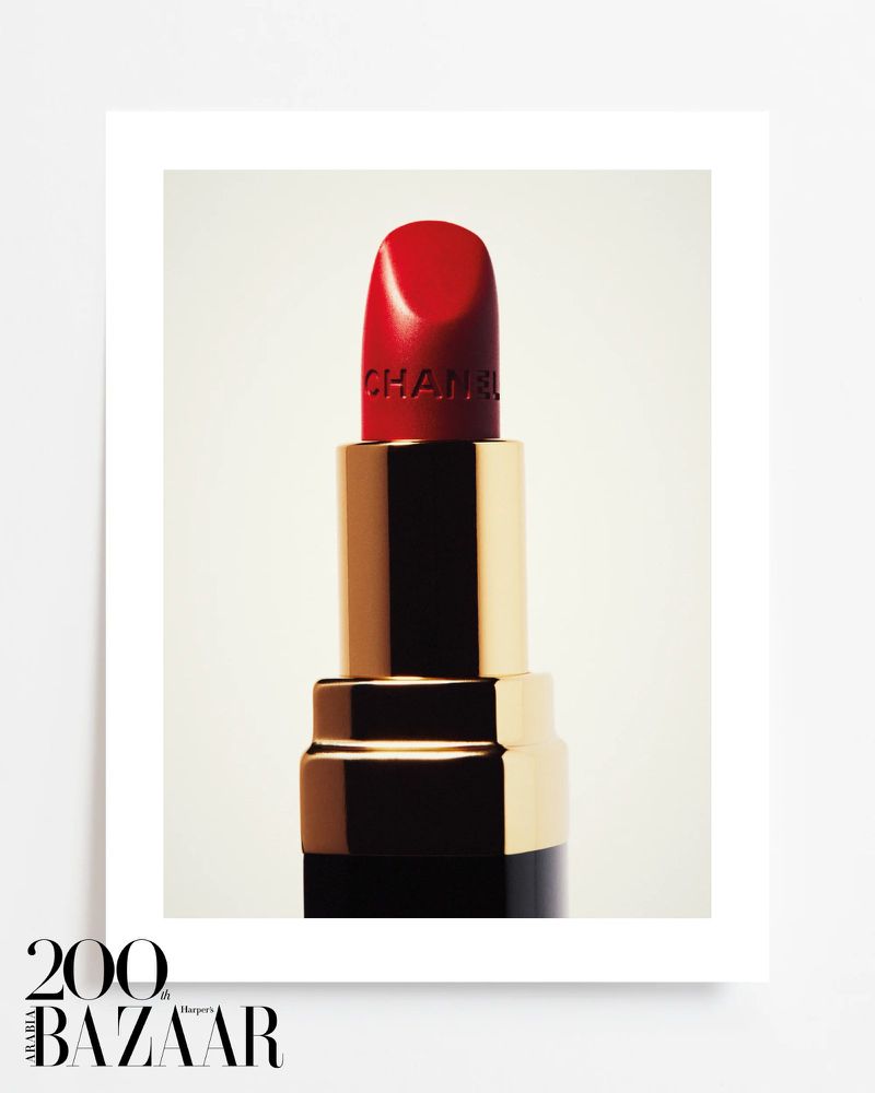 Close-up product shot of red Chanel lipstick with gold and black accents against a light backdrop, framed in a white border.
