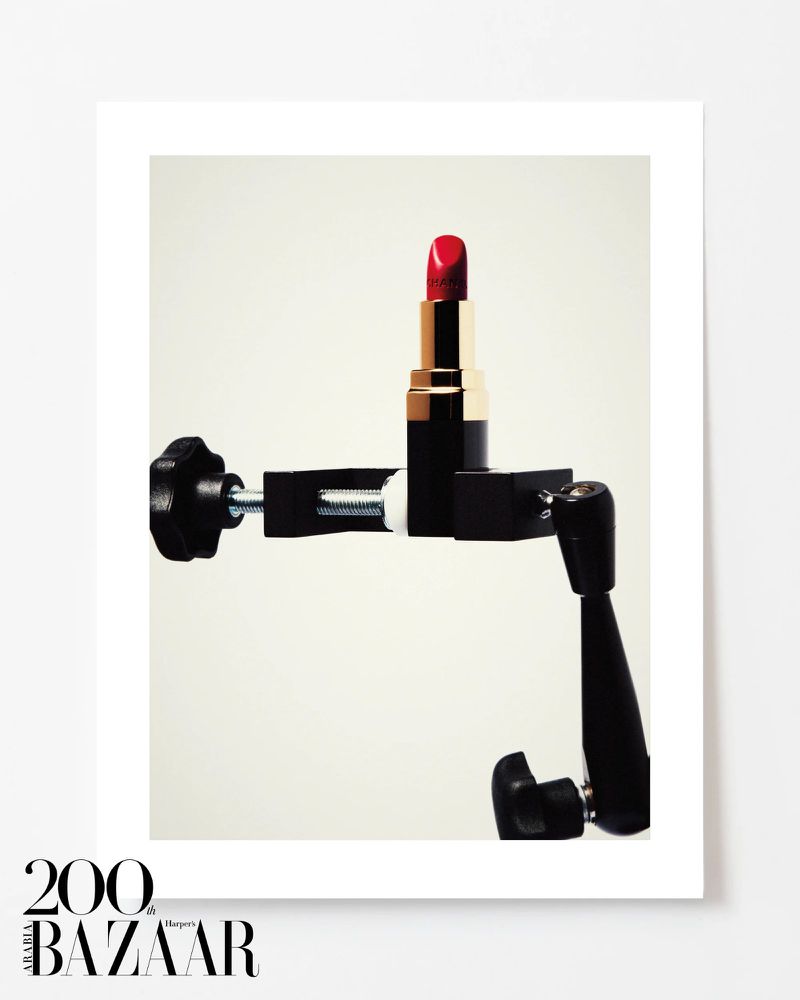 Close-up studio shot of a red lipstick tube held by a black clamp, showcasing beauty and cosmetics in a minimalist setting.