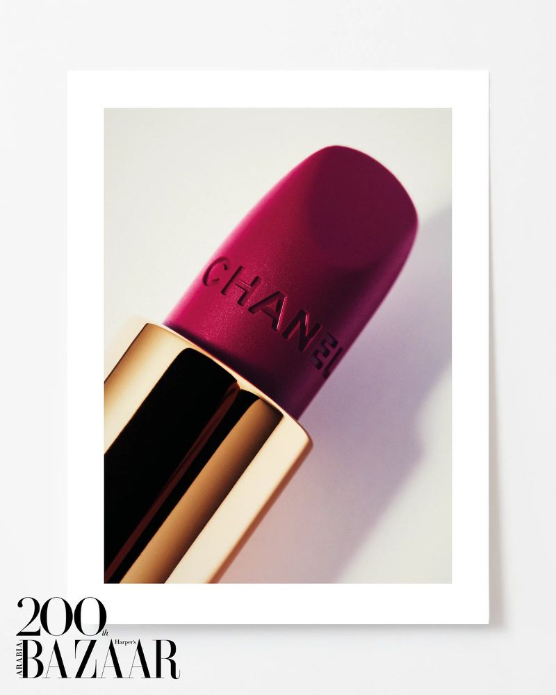 Close-up studio photograph of a Chanel lipstick tube featuring a gold base and deep pink lipstick with the brand name engraved.