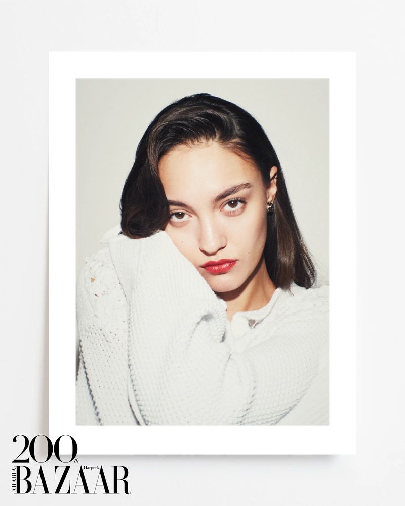Portrait of a model wearing a white knit cardigan with bold red lipstick against a plain white studio background.